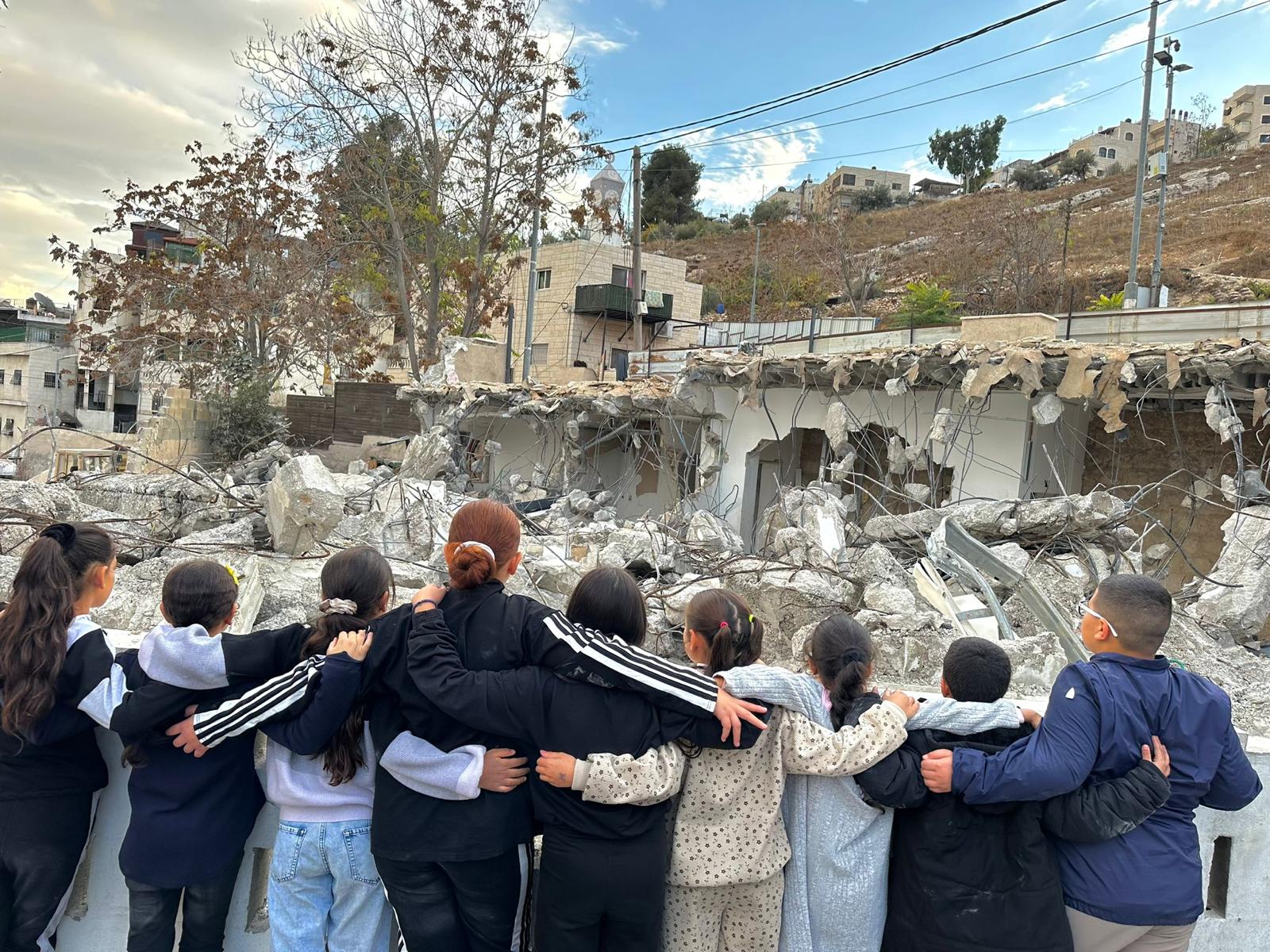 Community members standing together facing demolished buildings in Silwan